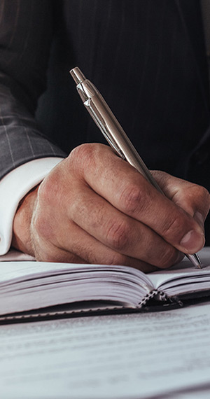 Man in business suit writes in ledger with silver ink pen at office desk.